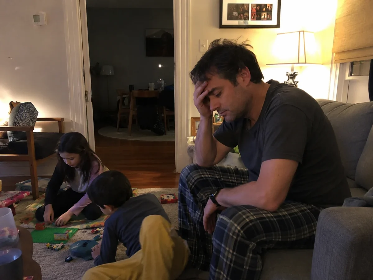 Exhausted man sitting on the couch in the evening, too drained to spend time with his kids